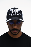 Gorra trucker blanca con detalles negros, diseño de aves y logo Iterniti bordado en el frente